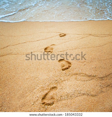 Footprints on the beach near the surf wave