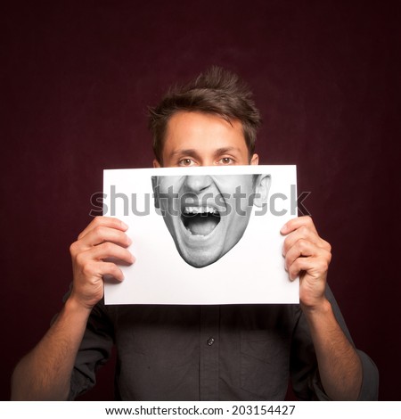 Young man with a half face portrait printed on a sheet of paper covering face, happy emotion