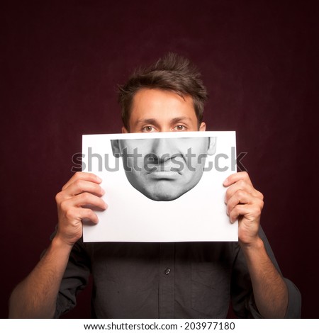 Young man with a half face portrait printed on a sheet of paper covering face, sad emotion