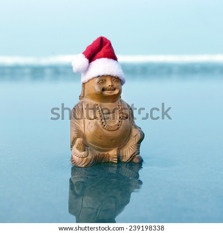 Budda statuette in the christmas bonnet on the beach. Blue waves in the background.