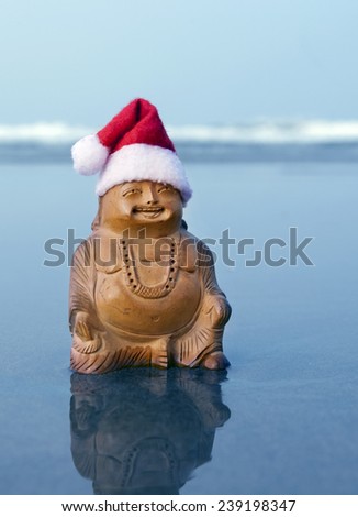 Budda statuette in the christmas bonnet on the beach. Blue waves in the background.
