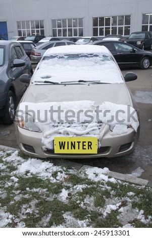 car covered with snow on the street with a yellow \'winter\' label instead of the number