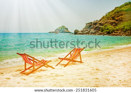 Two lounge chairs on the bay beach with rocks on the background