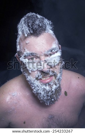 Russian extreme: a naked man in the snow with frozen beard and hair in the clouds of steam