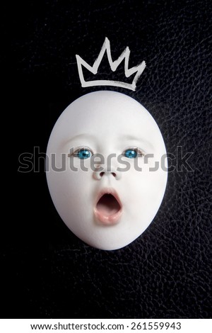 White egg with a baby face and crown on a black background