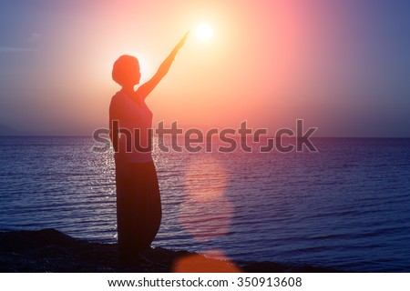 Silhouette of young girl standing on the beach with hand up, at the sunset against the sun