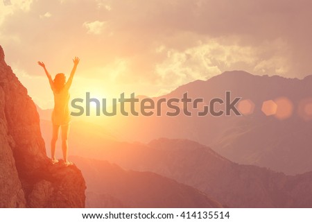The young girl raised her arms up to the sun on a background of mountains and sky with clouds