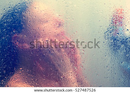 Beautiful woman in the shower behind glass with drops