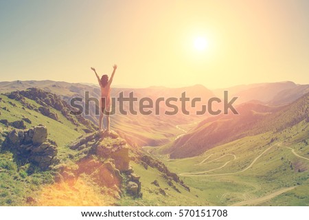 The young girl raised her arms up to the sun on a background of mountains