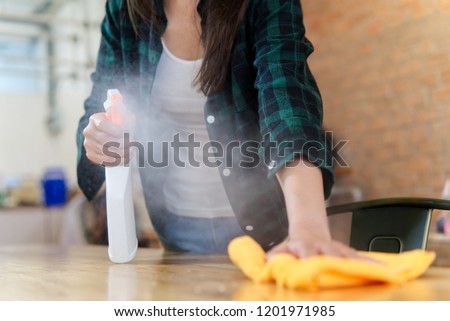 Close up view of woman cleaning a house. She is wiping dust using a spray and a orange fabric while cleaning on the table. Focus on the foggy. Happy house cleaning concept.