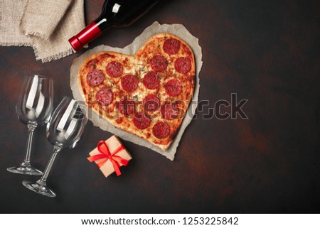 Heart shaped pizza with mozzarella, sausagered, wine bottle, two wineglass, gift box on rusty background. Top view.