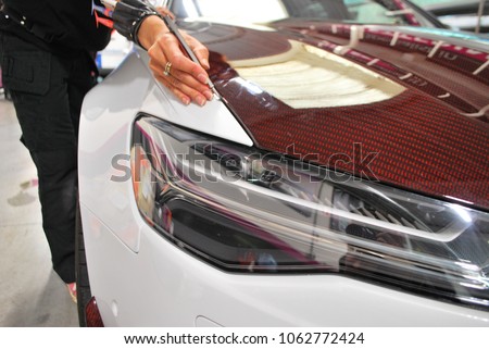 Car wrapping specialists straightening vinyl foil or film to remove ari bubbles cut carbon film