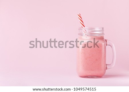 Strawberry smoothie or milkshake in mason jar on pink pastel background. Healthy food for breakfast and snack.