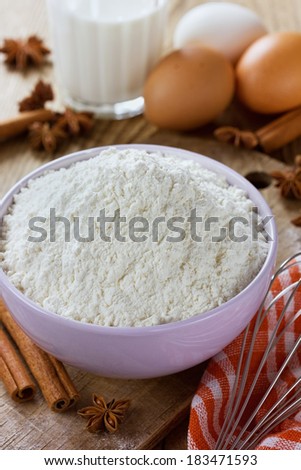 Flour in a ceramic bowl with eggs, milk, cinnamon sticks and anise star on a old wooden table, rustic style
