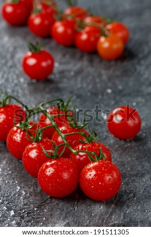 Cherry tomatoes on vine in water drops on a stone black table