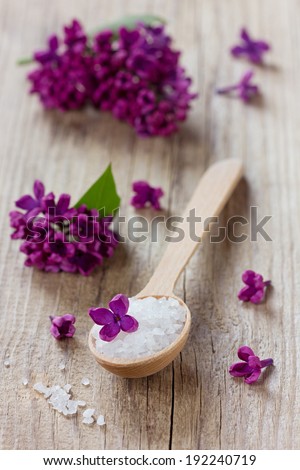 Spa composition with sea salt bath in wooden spoon and lilac flowers on a rustic surface, aromatherapy concept