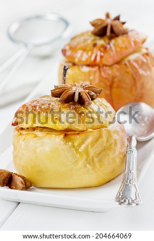 baked apples with honey, curds, raisins and nuts in a white plate decorated icing sugar and anise star on a wooden background