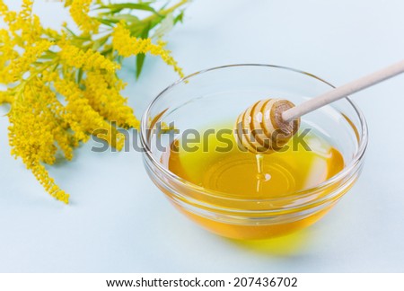 honey drip from a wooden honey dipper in glass bowl on blue background, selective focus on a honey dipper