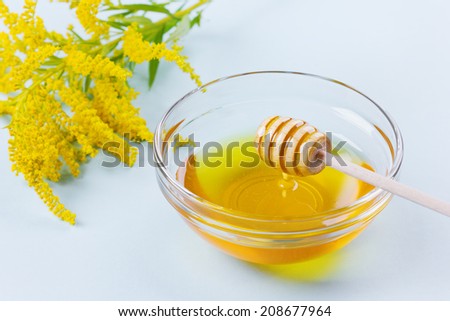 honey drip from a wooden honey dipper in glass bowl on a blue background, selective focus on a honey dipper