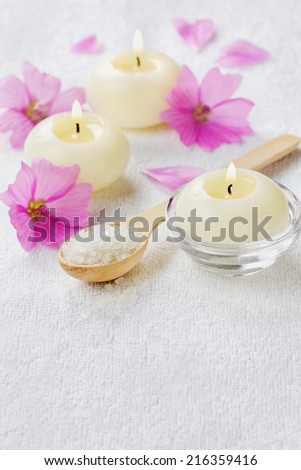 spa composition with sea salt bath in wooden spoon, pink flowers and burning candles on a white surface, aromatherapy concept