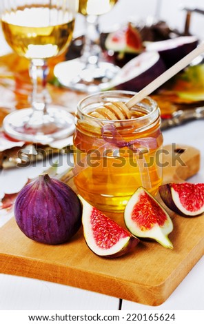 honey in jar, white wine in glasses and ripe fig on wooden board and vintage silver tray decorated autumn leaves