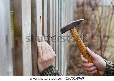 man hands drive nail with a hammer in wooden fence, carpentry