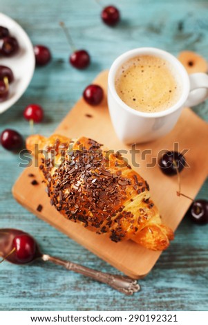 Tasty breakfast with fresh croissant, coffee and cherries on a wooden table, selective focus on croissant