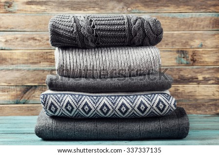 Pile of knitted winter clothes on wooden background, sweaters, knitwear, space for text