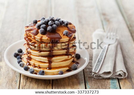 Stack of baked pancakes or fritters with chocolate sauce and frozen blueberries in a white plate on a wooden rustic table, delicious dessert for breakfast