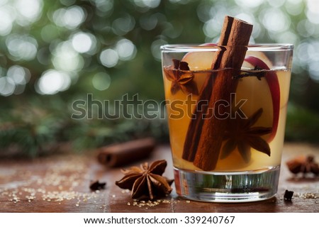 Christmas mulled apple cider with spices cinnamon, cloves, anise and honey on rustic table, traditional drink on winter holiday, magical evening light, selective focus