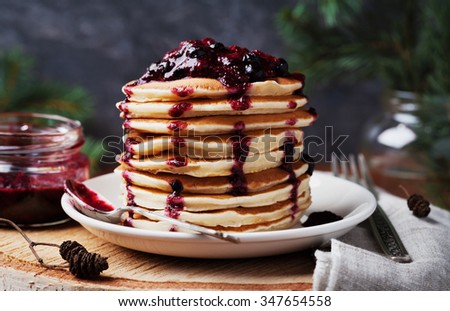 Stack of american pancakes or fritters with strawberry and blueberry jam in white plate on wooden rustic table decorated Christmas tree, delicious dessert for breakfast in winter, vintage style