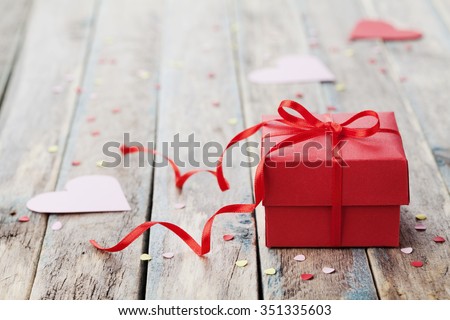 Gift box with red bow ribbon and paper heart on wooden table for Valentines day