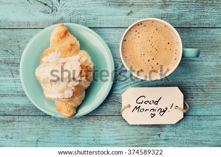 Coffee mug with croissant and notes good morning on turquoise rustic table from above, cozy and tasty breakfast, vintage toned