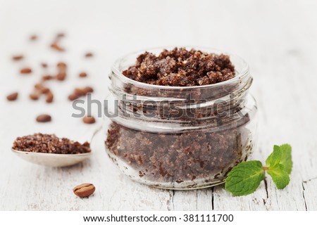 Body scrub of ground coffee, sugar and coconut oil in glass jar on white rustic table, homemade cosmetic for peeling and spa care