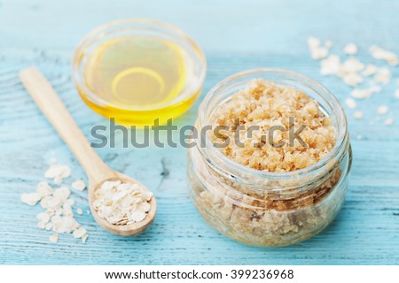 Body scrub of oatmeal, sugar, honey and oil in glass jar on blue rustic table, homemade cosmetic for peeling and spa care