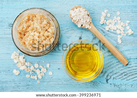 Body scrub of oatmeal, sugar, honey and oil in glass jar on blue rustic table, homemade cosmetic for peeling and spa care, top view