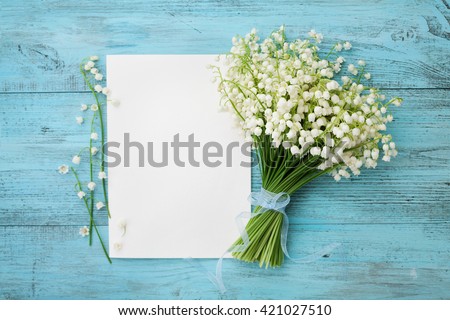 Bouquet of flowers lily of the valley and empty paper sheet on turquoise rustic table from above, beautiful vintage card, top view, copy space for text, flat lay