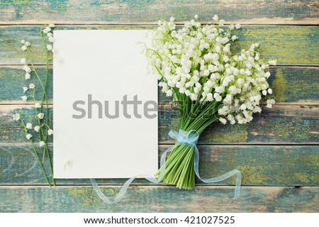 Bouquet of flowers lily of the valley and empty paper sheet on rustic table from above, beautiful vintage card, top view, copy space for text, flat lay