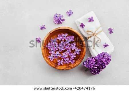 Spa and  wellness composition with perfumed lilac flowers water in wooden bowl and terry towel on gray stone background, aromatherapy, top view, flat lay