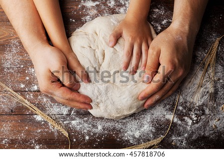 Father and child hands prepares the dough with flour, rolling pin and wheat ears on rustic wooden table from above. Homemade pastry for bread or pizza. Bakery background.