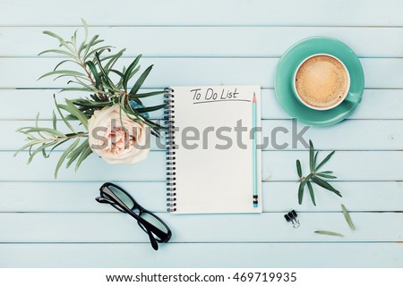 Morning coffee cup, notebook with to do list, pencil, eyeglasses and vintage rose flower in vase on blue rustic table from above. Planning and design concept. Cozy breakfast. Flat lay styling.