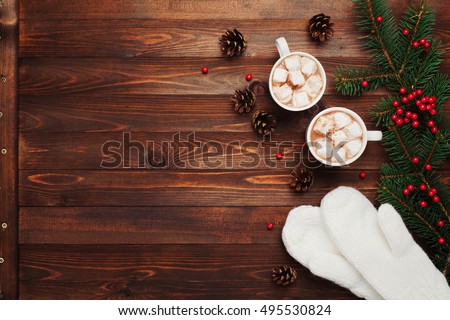 Two cups of hot cocoa or chocolate with marshmallow, mittens, christmas decor and fir tree on wooden rustic background from above. Flat lay style.