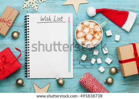 Cup of hot cocoa or chocolate with marshmallow, holiday decorations and notebook with wish list on turquoise vintage table from above, christmas planning concept. Flat lay style.