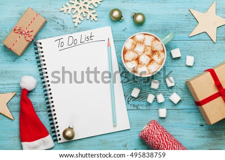 Cup of hot cocoa or chocolate with marshmallow, holiday decorations and notebook with to do list on turquoise vintage table from above, christmas planning concept. Flat lay style.