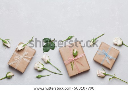 Gift or present box wrapped in kraft paper and rose flower on gray table top view. Flat lay styling. Copy space for text.