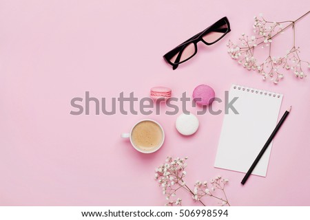 Coffee, cake macaron, clean notebook, eyeglasses and flower on pink table from above. Female working desk. Cozy breakfast. Flat lay style.