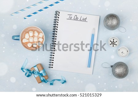 Cup of hot cocoa, gift, holiday decorations and notebook with to do list on blue vintage table from above, christmas planning and mockup. Flat lay style.