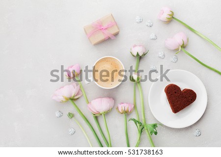 Breakfast for Valentines day with cup of coffee, gift, flowers and cake in shape of heart on gray table from above in flat lay style.