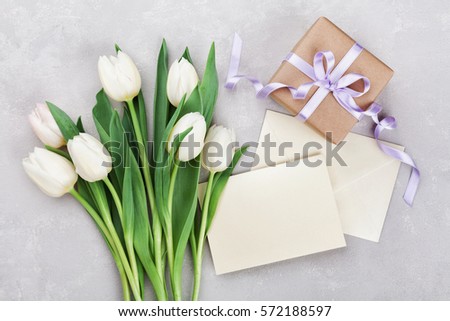 Spring tulip flowers, gift box and paper card on gray stone table from above in flat lay style. Greeting for Womens or Mothers Day.