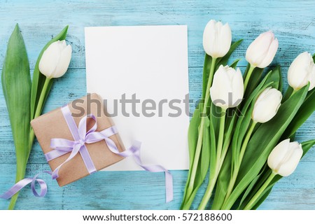 Spring tulip flowers, gift box and paper card on turquoise vintage table from above in flat lay style. Greeting for Womens or Mothers Day.